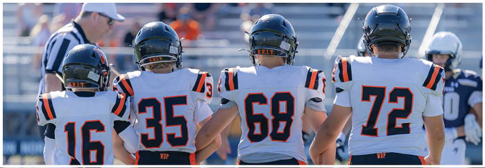 Four people wearing sports uniforms with numbers on the back stand on a field with a blue and white logo. Description generated by AI