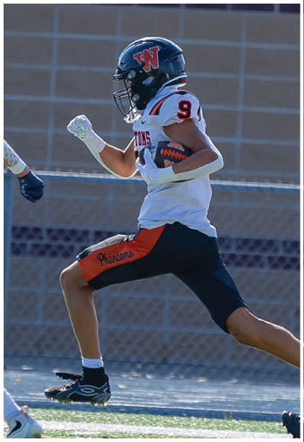 A person wearing a football uniform with a helmet is running on a field while holding a football. Description generated by AI