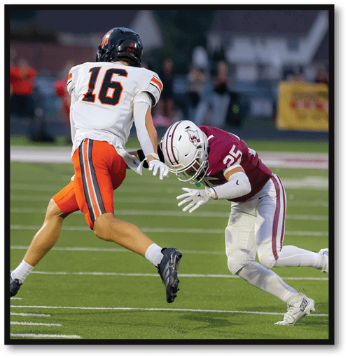 A person wearing a white and orange football uniform with the number 16 is running while another person in a maroon and white football uniform with the number 35 is attempting to tackle them on a football field. Description generated by AI