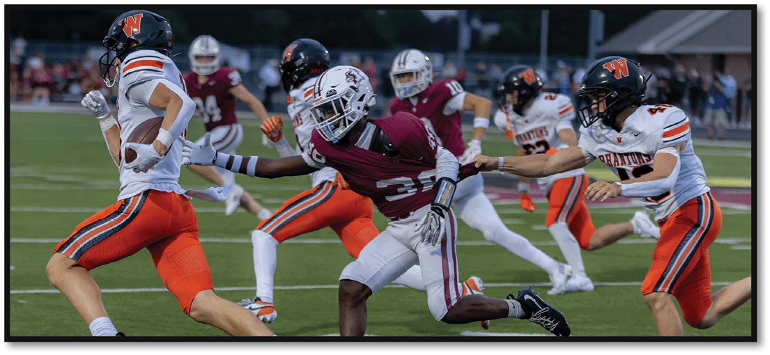 People wearing football uniforms are actively running and competing on a grassy field during a game. Description generated by AI