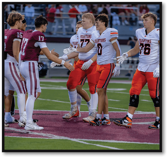 People in football uniforms from two different teams are shaking hands on a field after a game. Description generated by AI
