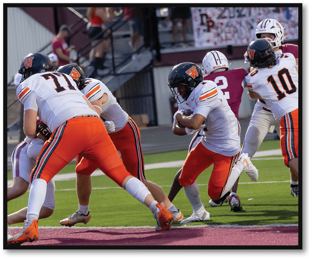 Adults wearing sports uniforms are engaged in a football game on a field near the end zone. Description generated by AI