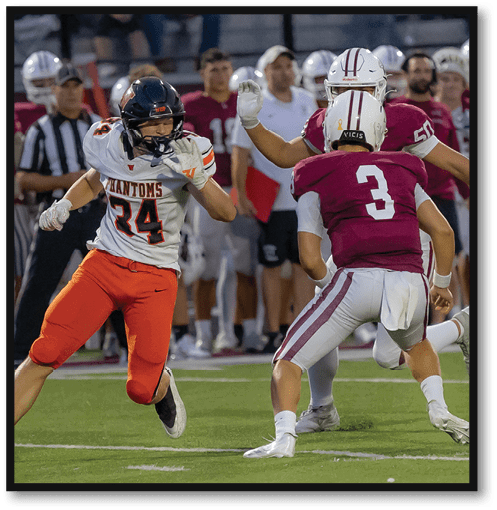 A person wearing an orange and white football uniform with the number 24 is running on a football field while other players and officials stand in the background. Description generated by AI