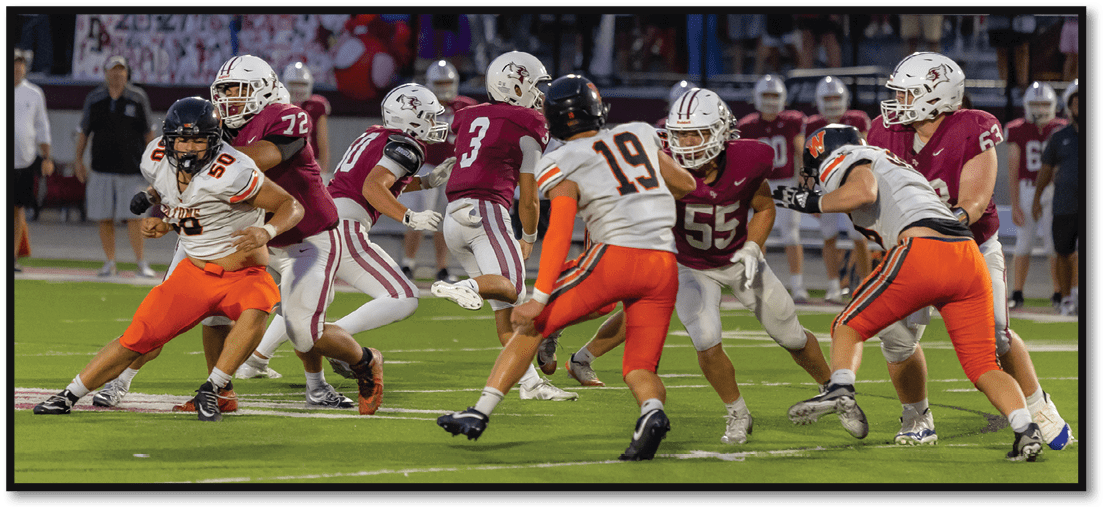 People in football uniforms are actively engaged in a play on a field with a crowd watching from the stands. Description generated by AI