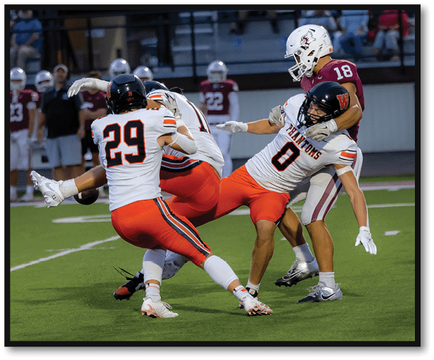 Two people in white and orange football uniforms are tackling a person in a maroon and white uniform on a football field. Description generated by AI