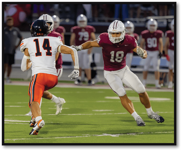 A person wearing a white and orange football uniform with the number 14 is running on a football field while being pursued by two people in maroon and white uniforms. Description generated by AI