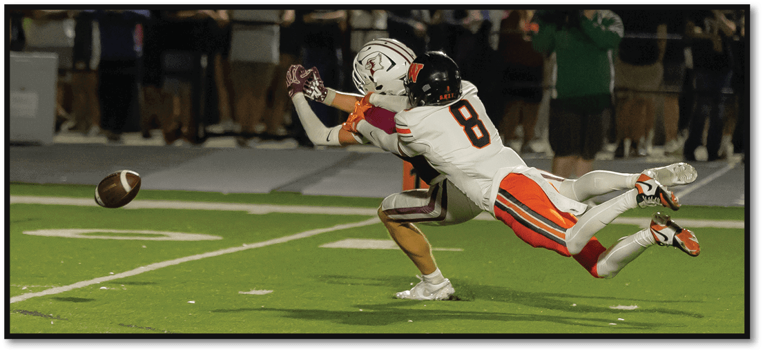 Two football players in action are diving to catch a football on a field with spectators in the background. Description generated by AI