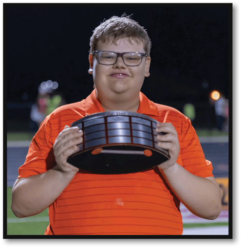 Person wearing glasses and an orange striped shirt is holding a trophy or award plaque while standing outdoors at night. Description generated by AI