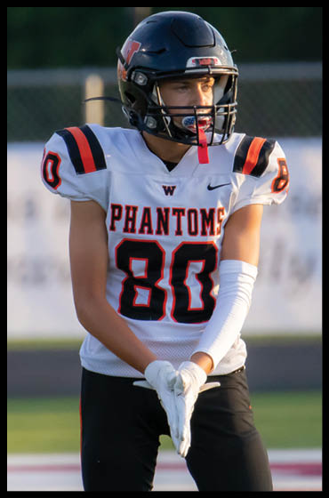 A person wearing a football uniform with the number 80 and the word “PHANTOMS" on the jersey is standing on a field with hands clasped together. Description generated by AI