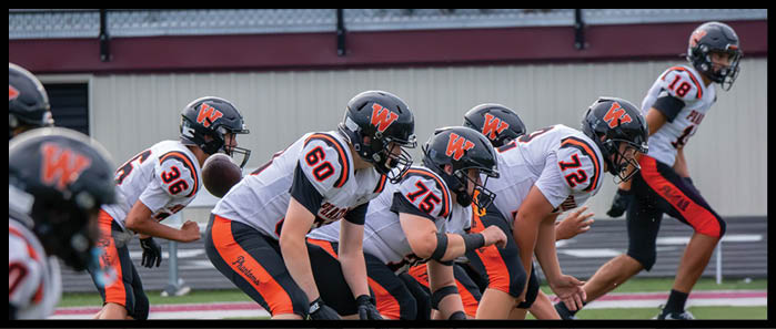 A group of people in football uniforms and helmets are lined up in a ready stance on a field, preparing for a play. Description generated by AI