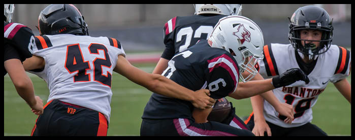 People wearing football helmets and uniforms are engaged in a game on a field. Description generated by AI