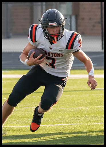 A person wearing a football uniform with a helmet is running on a field while holding a football. Description generated by AI