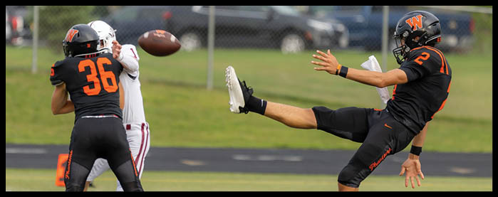 Two people in black football uniforms are playing against a person in a white uniform with a football in midair between them on a field. Description generated by AI