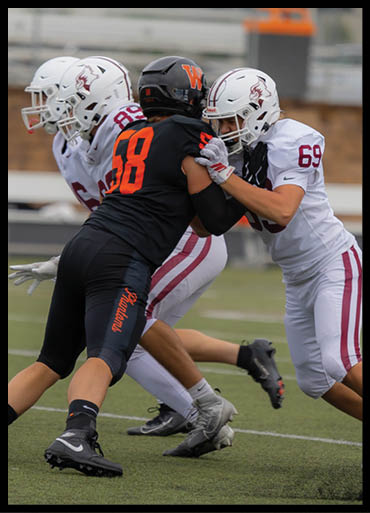 Two people in football uniforms are engaged in a blocking stance on a football field during a game. Description generated by AI