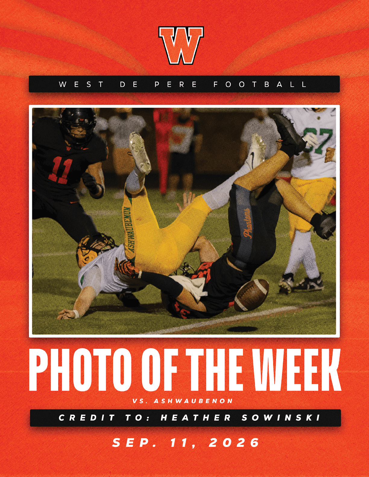 Two football players in yellow and black uniforms are tangled on the field with the ball loose nearby while other players stand in the background during a night game. Description generated by AI