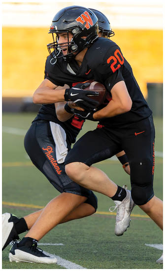 Two people in black football uniforms are engaged in a tackle on a green field, with one holding a football tightly. Description generated by AI