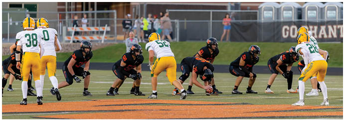 Two opposing American football teams are lined up on the field preparing for a play, with one team wearing black uniforms and the other team wearing white and yellow uniforms. Description generated by AI