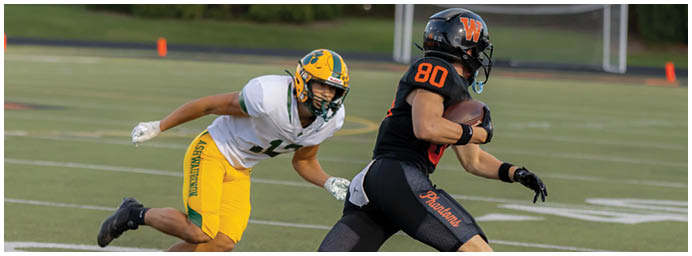 A person in black sportswear with the number 80 is running with a football while another person in yellow and white sportswear is chasing them on a football field. Description generated by AI