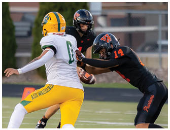 Two football players in black uniforms tackle a player in a white and yellow uniform holding a football on a field. Description generated by AI