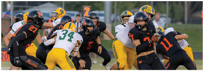 People wearing football helmets and uniforms in black and yellow are engaged in a play on a grassy field during a game. Description generated by AI