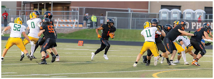 A group of people wearing sports uniforms are playing football on a field with one person running with the ball while others block or attempt to tackle. Description generated by AI