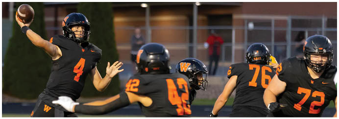 Two people in black and orange sports uniforms are actively playing football on a field. Description generated by AI