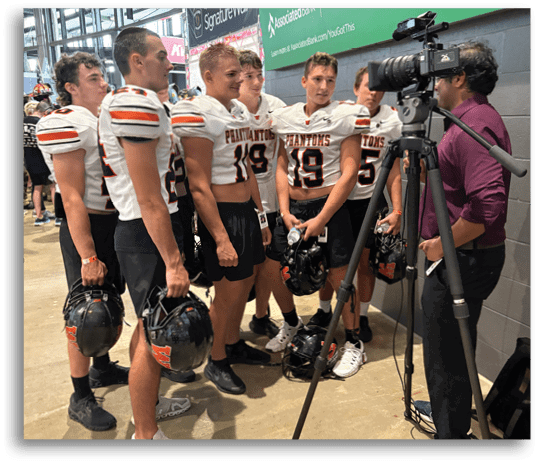 Five people wearing white football jerseys and black shorts are standing indoors holding black helmets. Description generated by AI