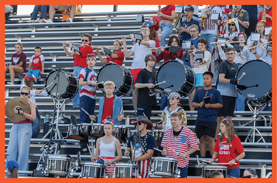 A group of people in casual clothing are playing musical instruments including drums and flutes while standing in bleachers. Description generated by AI