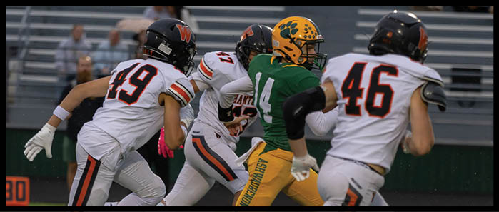 Five people in black football uniforms with orange numbers stand on a field facing three people in white football uniforms while two referees in black and white striped shirts stand nearby. Description generated by AI