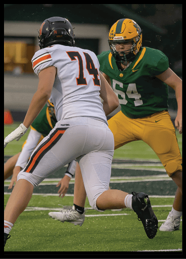 Two people in football uniforms are engaged in a play on a field, with one wearing a white jersey numbered 74 and the other in a green jersey numbered 64. Description generated by AI