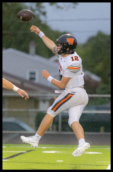 Two people in football uniforms are on a field, with one person in mid-air preparing to throw a football. Description generated by AI
