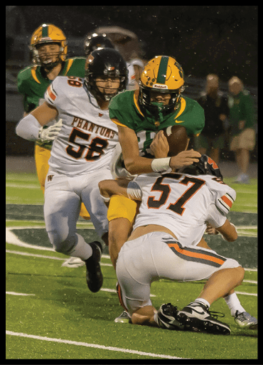 A person in a green and yellow football uniform is running with the ball while two people in white and black football uniforms attempt to tackle them on a field. Description generated by AI