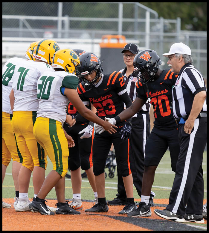 Several people in football uniforms and referees stand together on a field, with some players shaking hands. Description generated by AI
