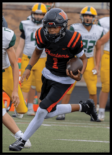 A person wearing a black and orange football uniform with the word Phantoms is running with a football on a field while other players in yellow and green uniforms are in the background. Description generated by AI