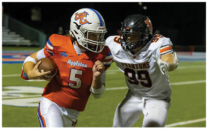 Two people in football uniforms are actively running on a field, with one holding a football and the other attempting to catch or tackle. Description generated by AI