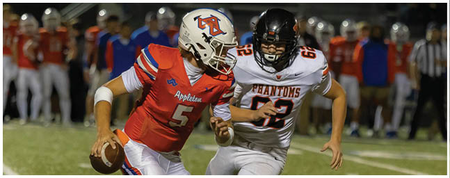 Two people in football uniforms are actively playing on a field with one holding a football and the other attempting to block or tackle. Description generated by AI
