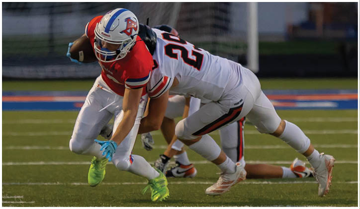 Two people in football uniforms are engaged in a tackle on a field near a goalpost. Description generated by AI
