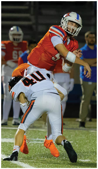Four people in white football uniforms with black helmets are celebrating on a field with blue and orange markings at night. Description generated by AI