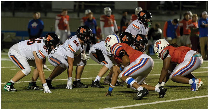 Two opposing American football teams in helmets and uniforms are lined up facing each other on a field during a game. Description generated by AI