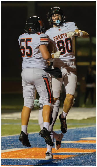 Two people in football uniforms jump and celebrate on a field near the end zone during a nighttime game. Description generated by AI