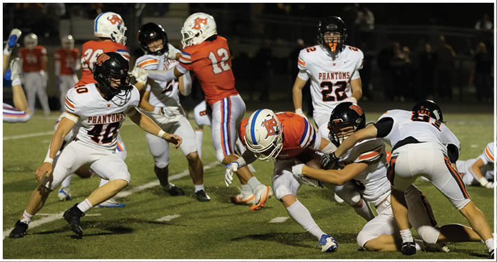 A group of people wearing football uniforms are actively engaged in a play on a grassy field during a nighttime game. Description generated by AI