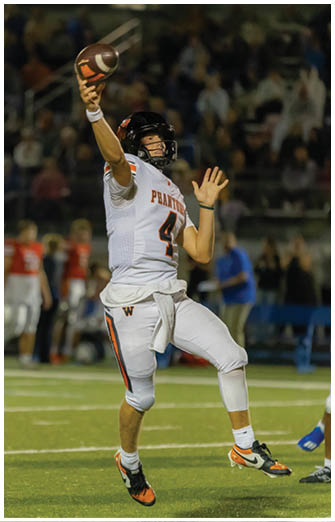 A person wearing a white football uniform with the number 4 is in mid-throw with a football on a field during a game. Description generated by AI