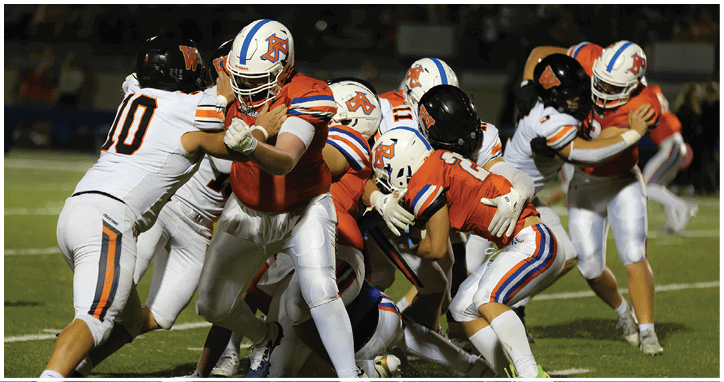 Several people in football uniforms are engaged in a play on a grassy field under stadium lights. Description generated by AI