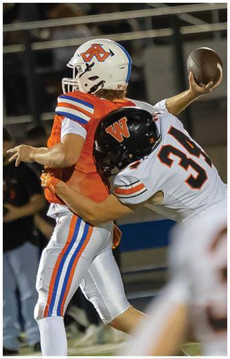 Two people in football uniforms are engaged in a play with one holding a football and the other attempting to tackle. Description generated by AI