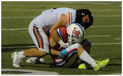 Two people in football uniforms are on a field with one person tackling the other who is holding a football. Description generated by AI