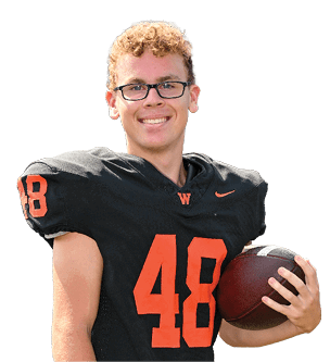 A person with curly hair and glasses is smiling while wearing a black football jersey with the number 48 and holding a football. Description generated by AI