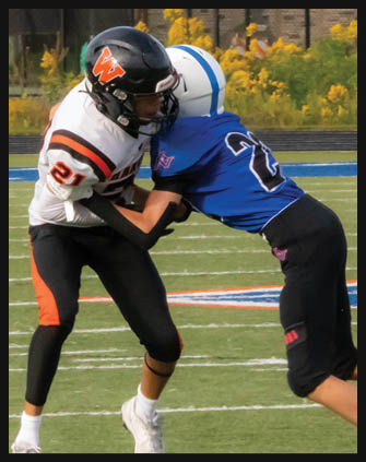Two people in football uniforms are engaged in a tackle on a grassy field with yard lines and colorful markings. Description generated by AI