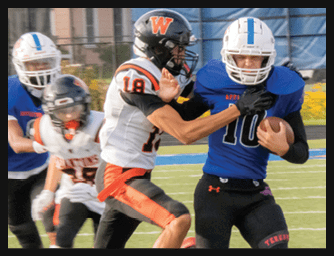People wearing football uniforms are actively engaged in a play on a field with one person in a blue jersey holding the ball while others in white and orange jerseys attempt to tackle. Description generated by AI