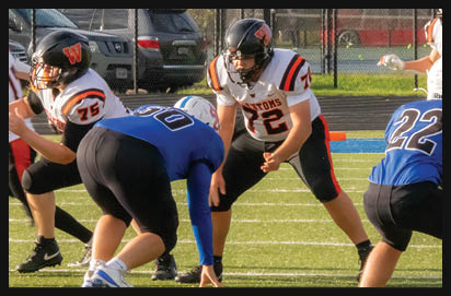 People in football uniforms are positioned on a field, preparing for a play during a game. Description generated by AI