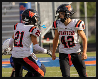 Two people in football uniforms with helmets are on a field, one wearing number 21 and the other number 42 with “PHANTOMS" on the jersey. Description generated by AI